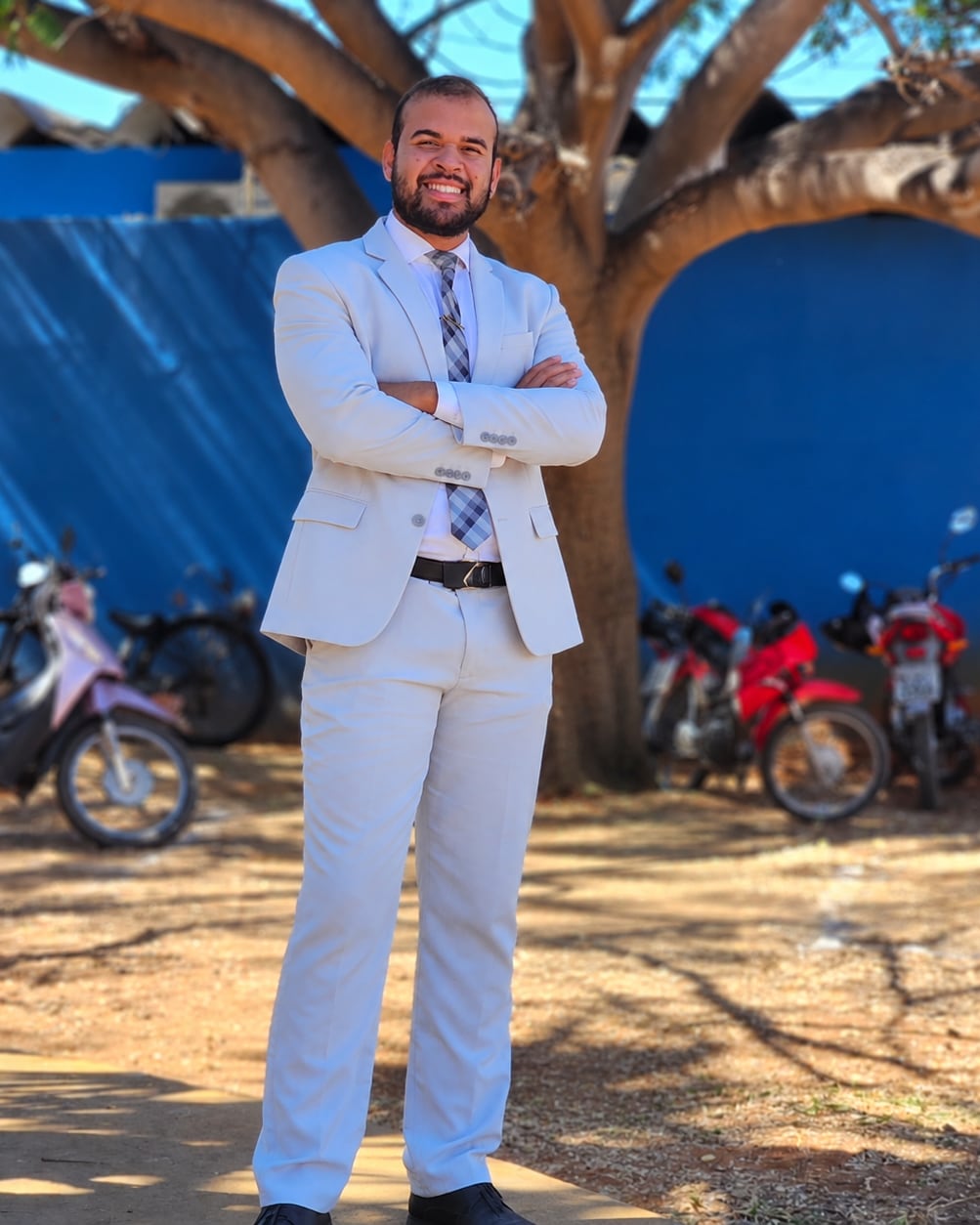 Kevinn Ribesi de terno claro e braços cruzados, sorrindo ao ar livre