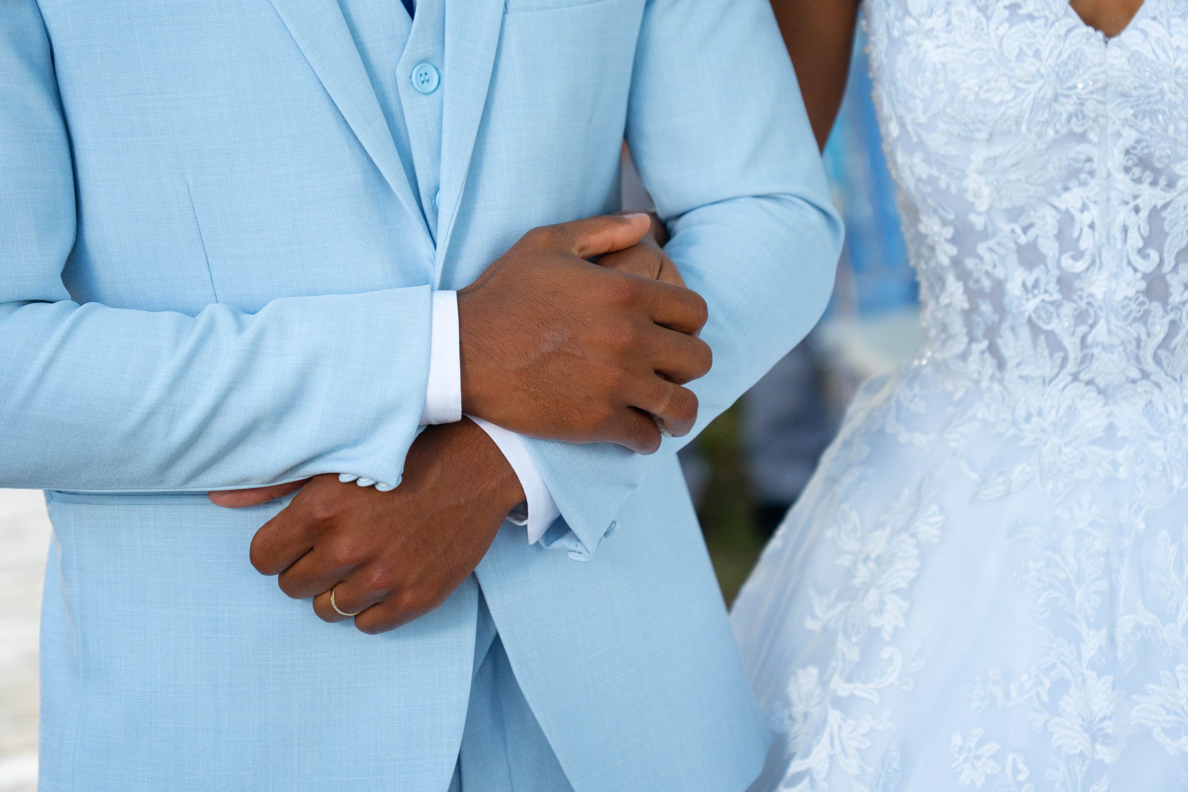 Detalhe das mãos do noivo e do vestido da noiva